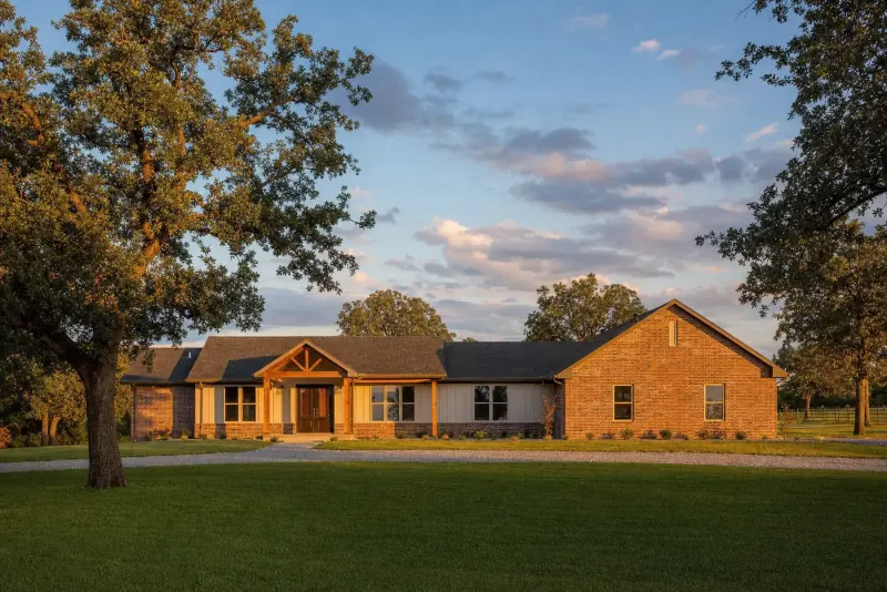 A brick ranch house with a wide lawn and large oak trees at golden hour